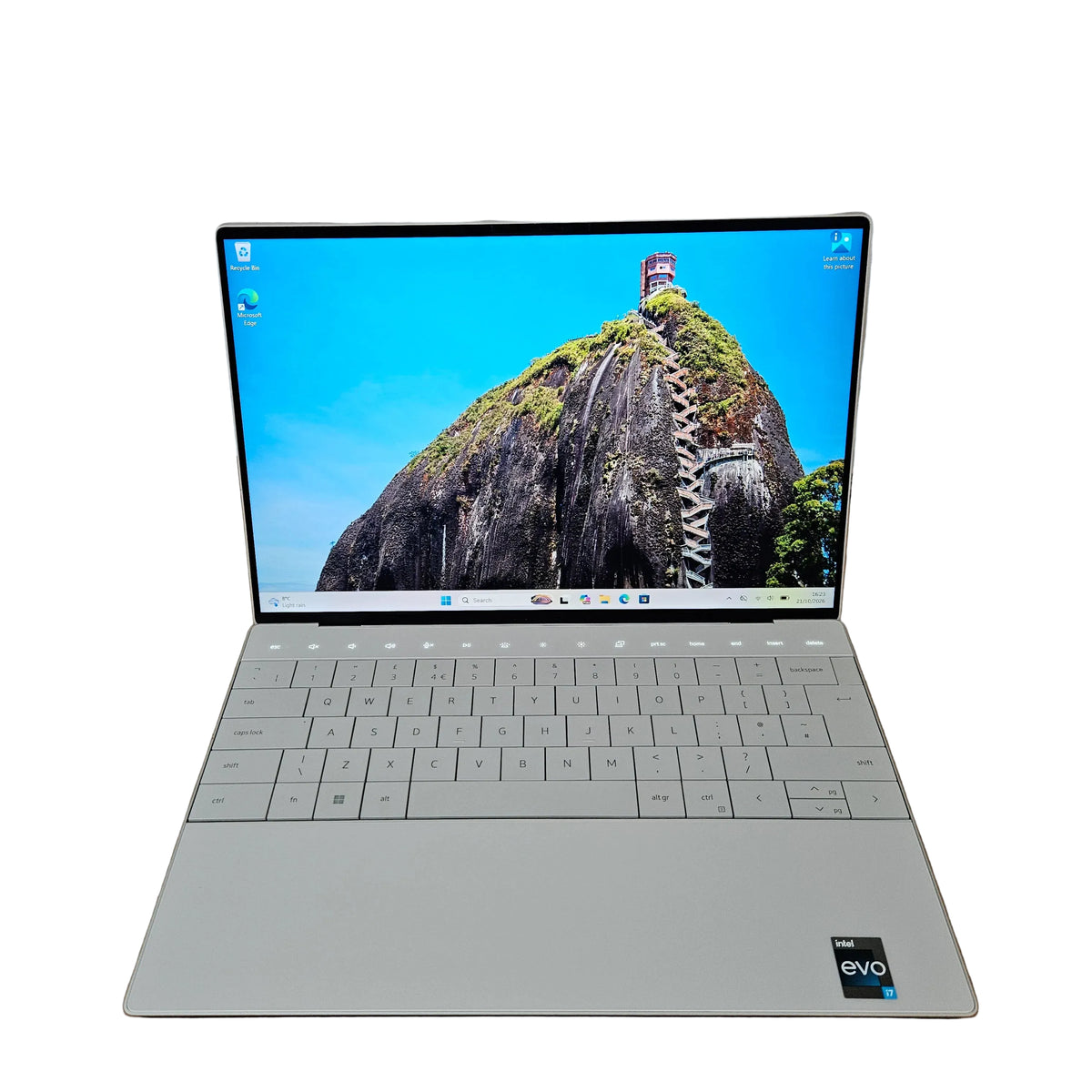 A silver dell xps 9320 EVO laptop is open and resting on a cardboard box, set against a plain wall and carpet background.
