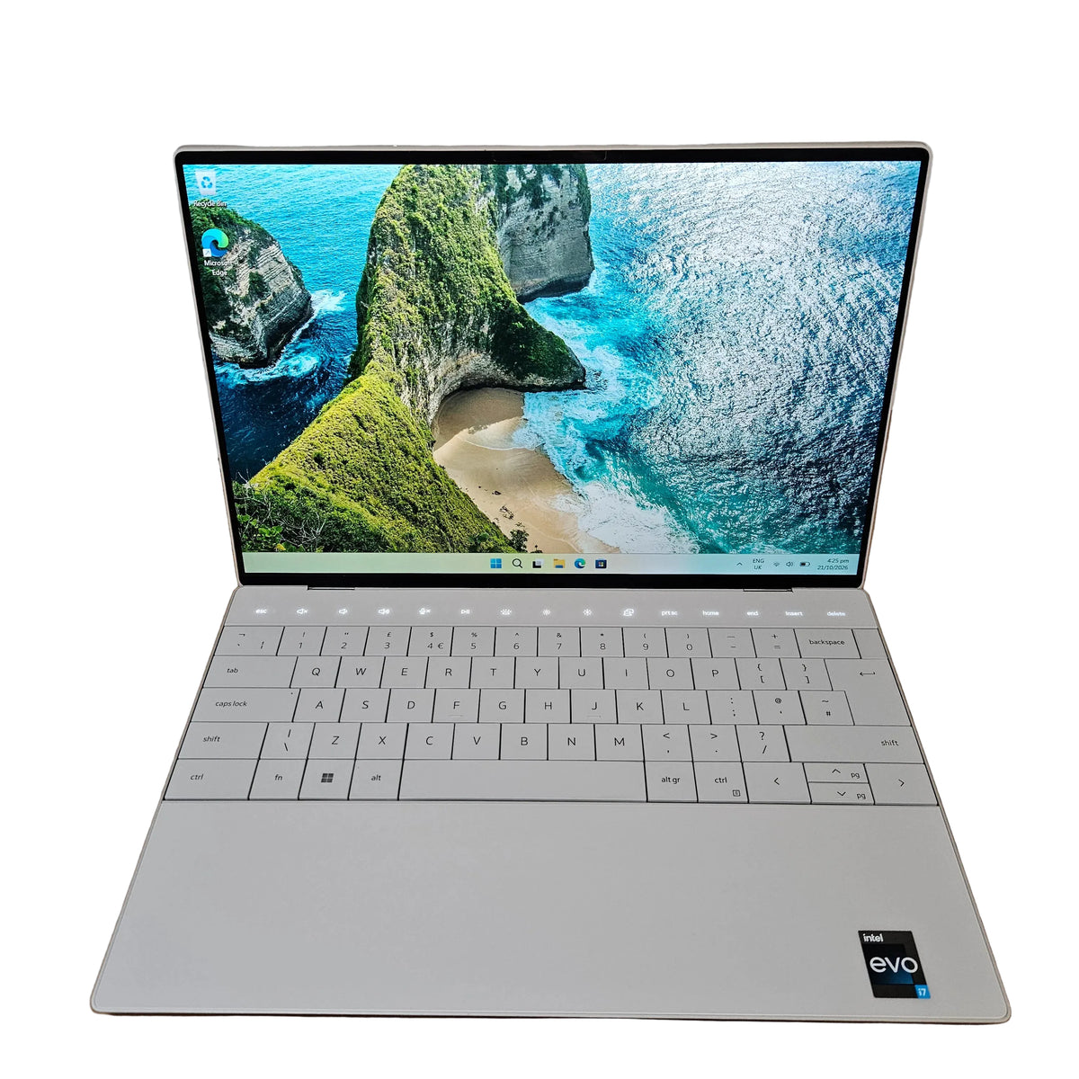 A silver dell xps 9320 laptop is open and placed on a cardboard box on a carpeted floor against a white wall. The screen displays a scenic wallpaper of a coastal cove.