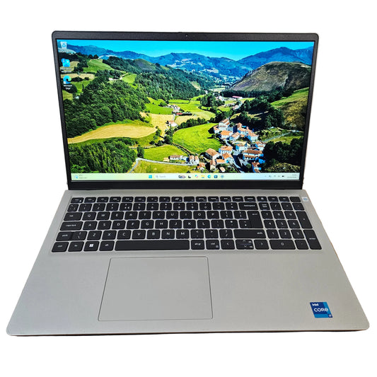 An open silver laptop with a black keyboard and screen, showing a mountain landscape wallpaper. The laptop is placed on a brown cardboard box on a gray carpet against a white wall.
